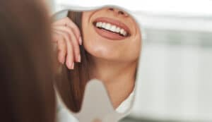 happy young woman smiling checking out her perfect healthy teeth mirror close up dentist office Blog